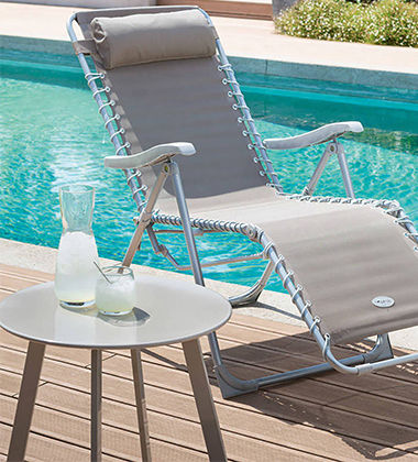 Petite table ronde avec pieds en bois à côté d'un transat et d'une piscine