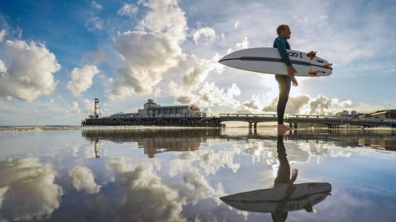 A surfer walking past Boscombe Pier at low tide