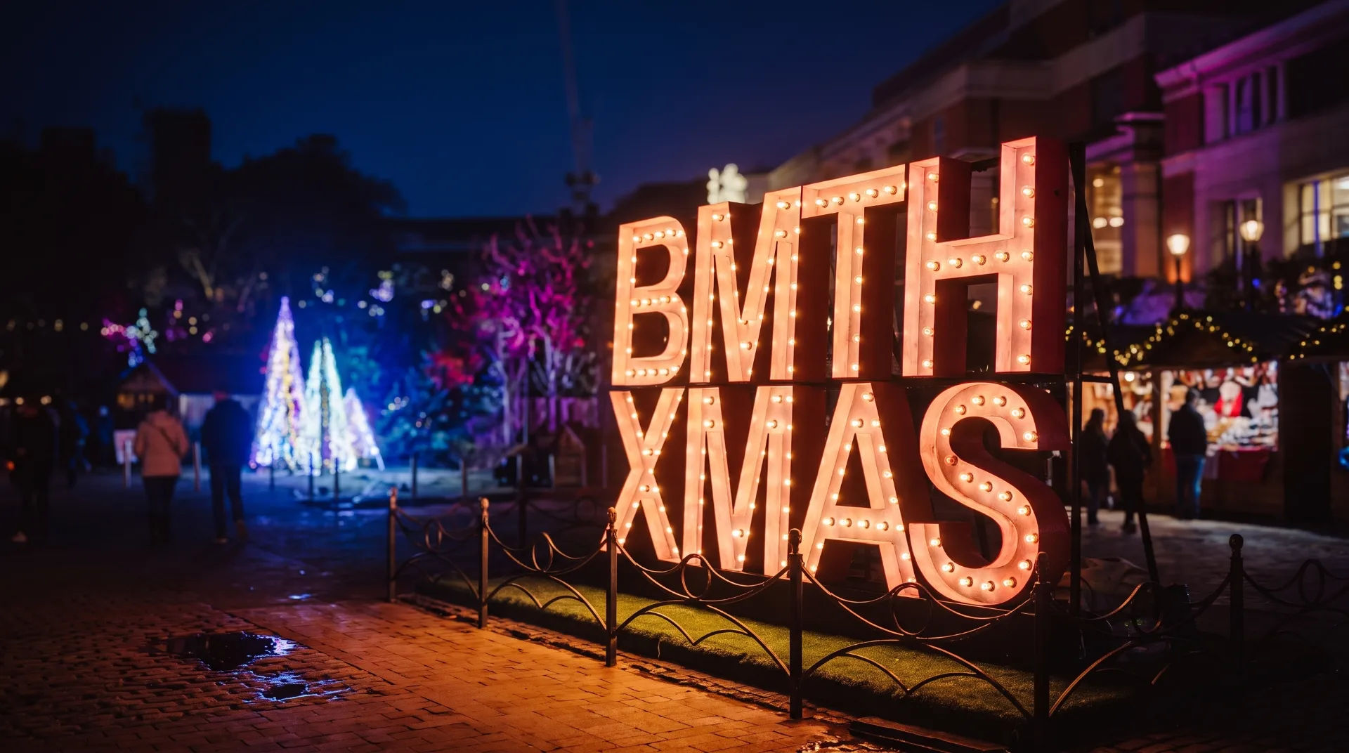 Illuminated sign reading 'BMTH XMAS' with festive lights and trees in the background at a Christmas market