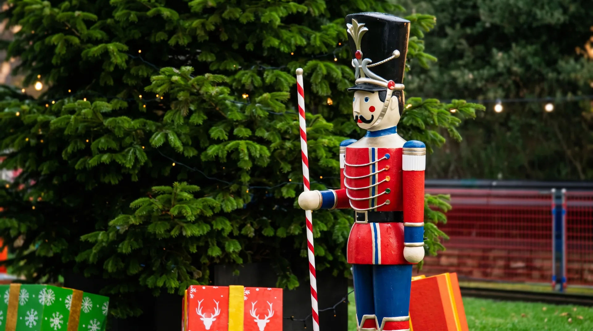 A colourful wooden nutcracker soldier stands beside brightly wrapped presents and a decorated Christmas tree.