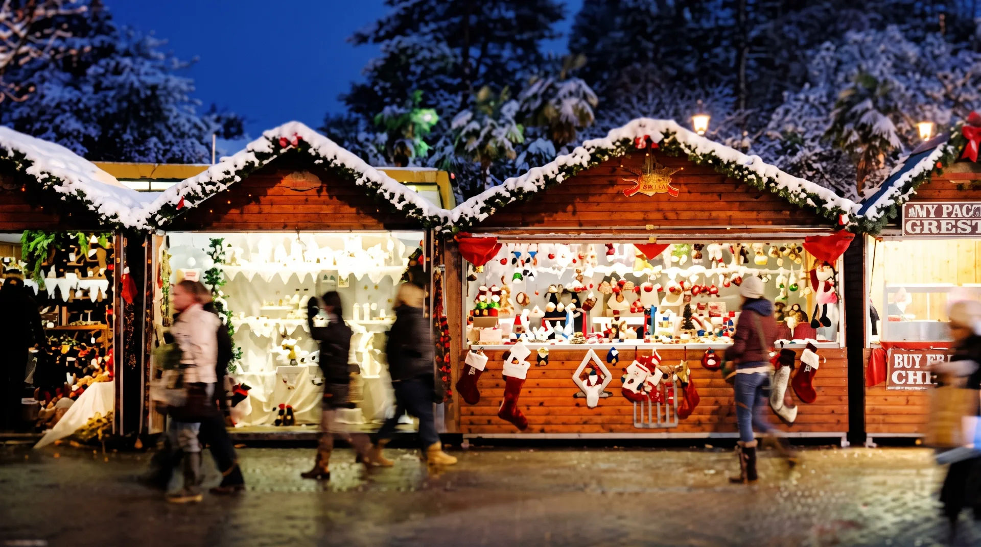 Wooden Christmas market stalls adorned with snow and festive decorations, with people walking by in winter attire.