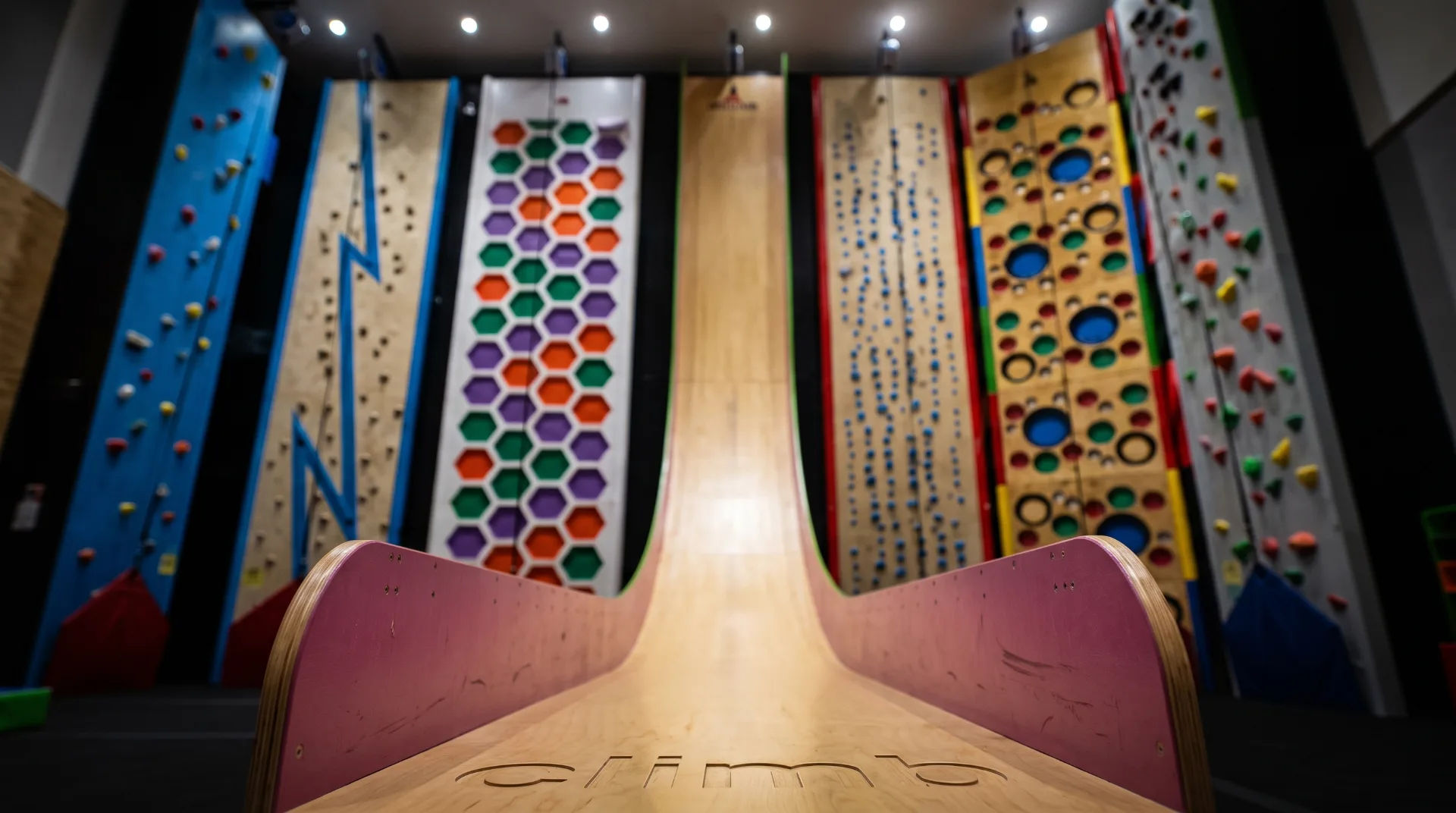 Indoor climbing walls with various colourful designs and a wooden ramp in the foreground at RockReef