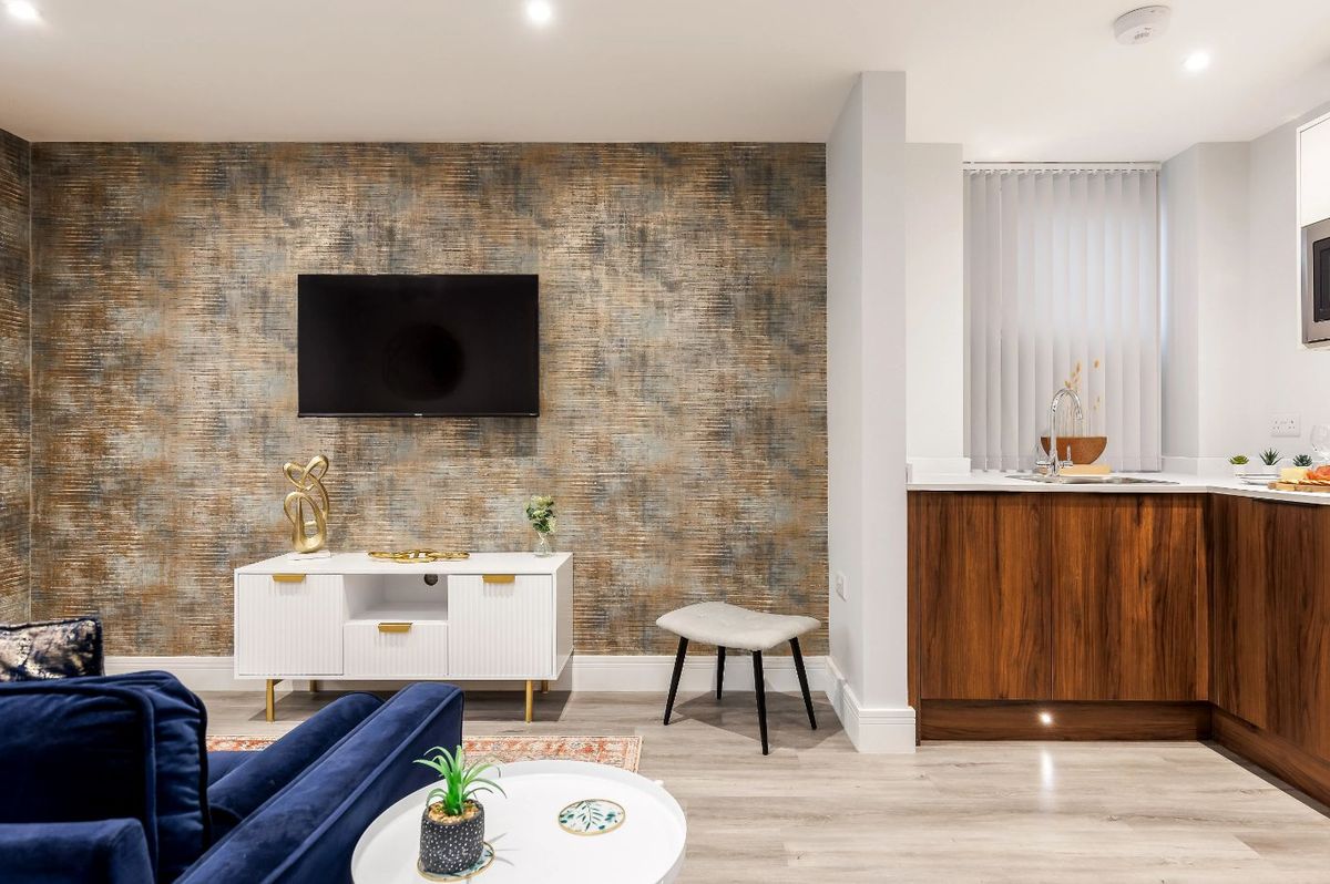 Stylish living area with a blue sofa, modern TV, and kitchen area featuring wooden cabinets