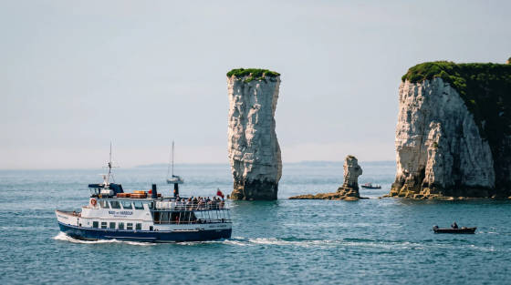 A boat sailing past Old Harry Rocks with cliffs in the background