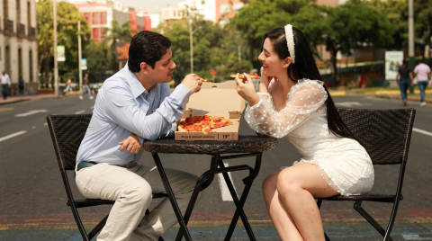 A couple sharing pizza at a small table on the street