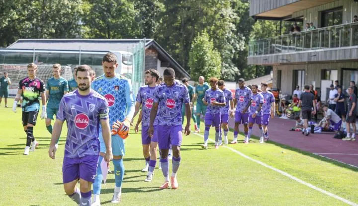 AFC Bournemouth players in purple kits walk onto the pitch before a match, with spectators in the background.
