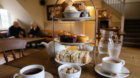 A tiered stand with sandwiches, cakes, and scones on a wooden table