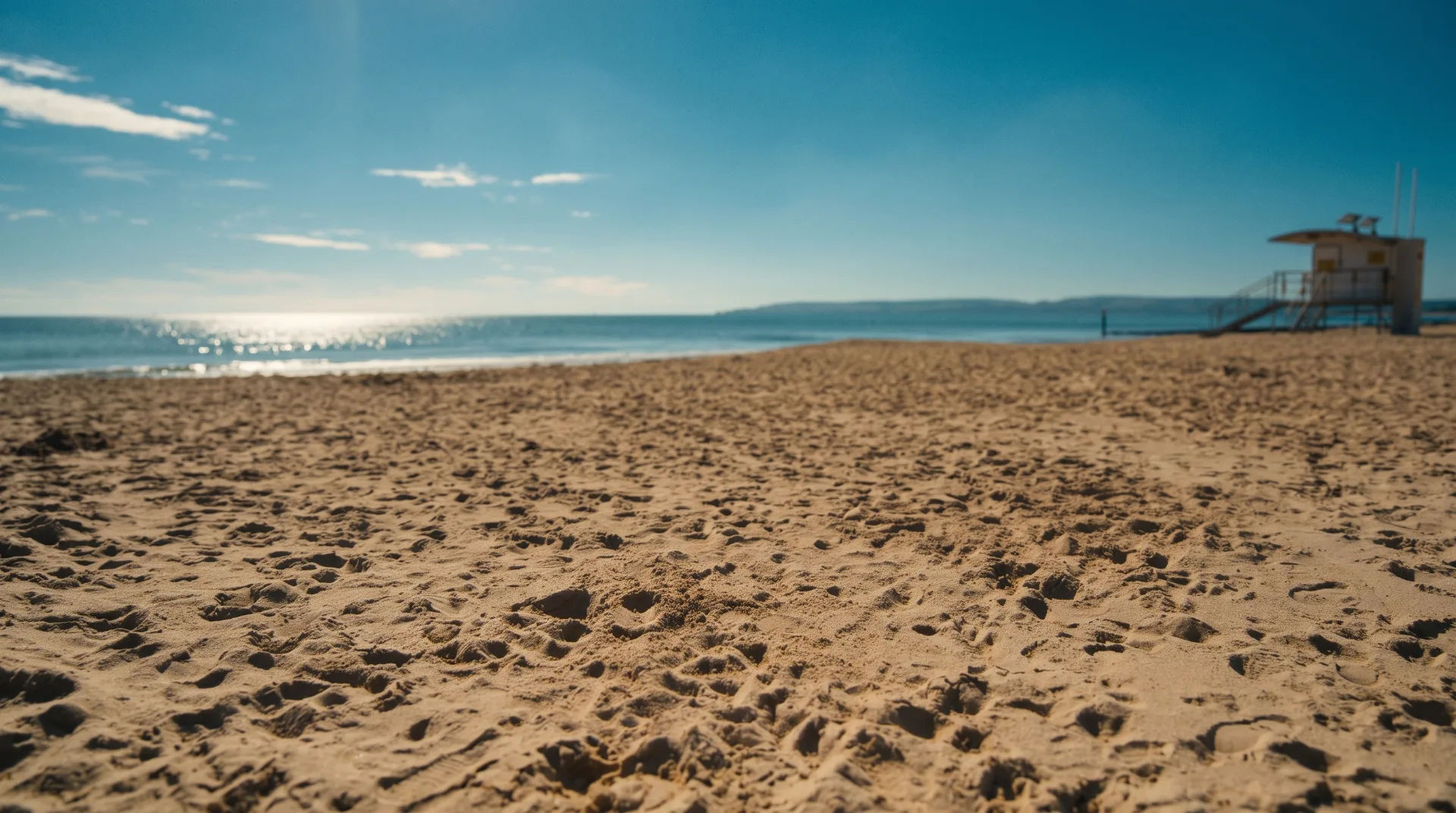 Sandy beach with gentle waves under a clear blue sky, lifeguard station in the background
