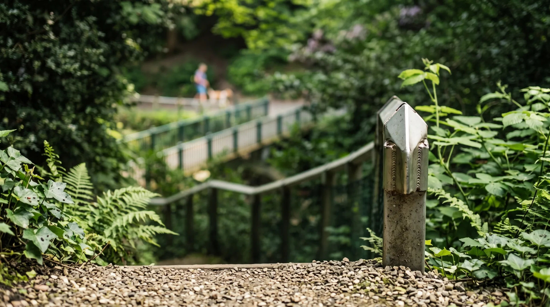 A winding path through lush greenery, with a metal railing and pebbled ground in the foreground.