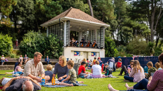 People enjoying an outdoor concert on the grass near a bandstand