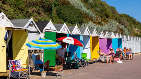 Row of colourful beach huts with sun umbrellas and people relaxing