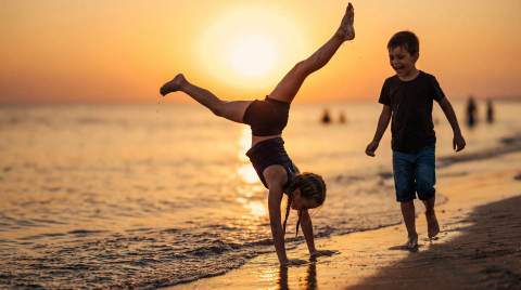 Two children playing on the beach during sunset