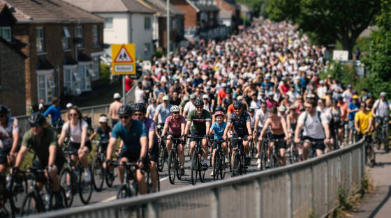 A large group of cyclists riding on a road with houses nearby