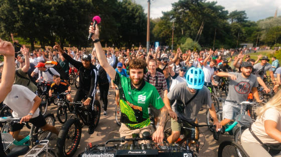 A large group of cyclists raising their hands in a park