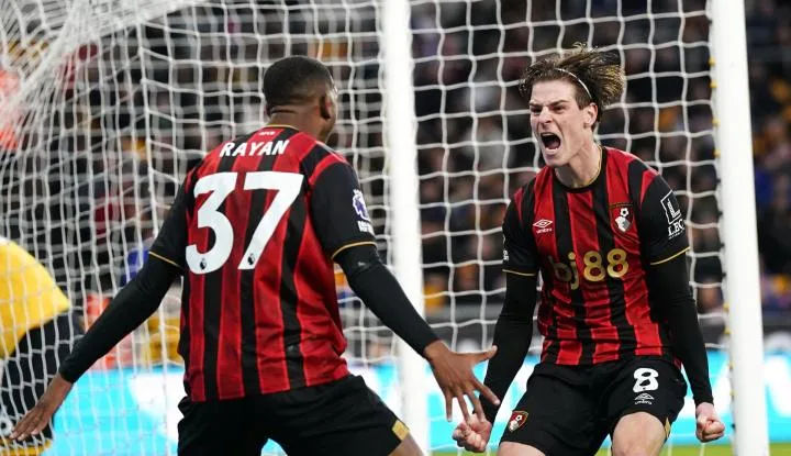 Two Bournemouth players celebrating a goal, one with a red and black striped jersey and the other wearing a black jersey with red stripes.