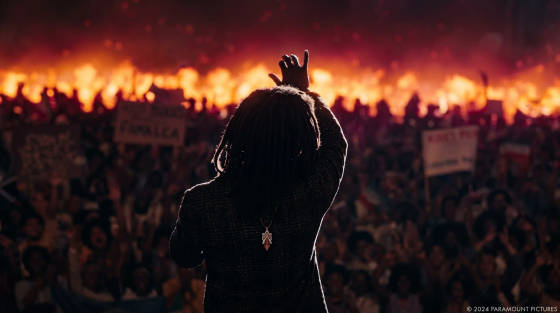 A silhouetted speaker with dreadlocks gesturing towards a crowd