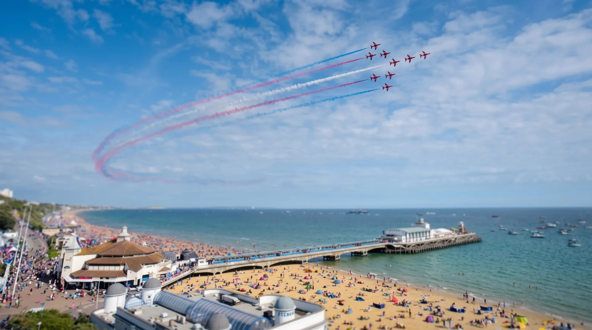 Red and blue smoke trails from planes flying over a busy Bournemouth beach and pier on a sunny day