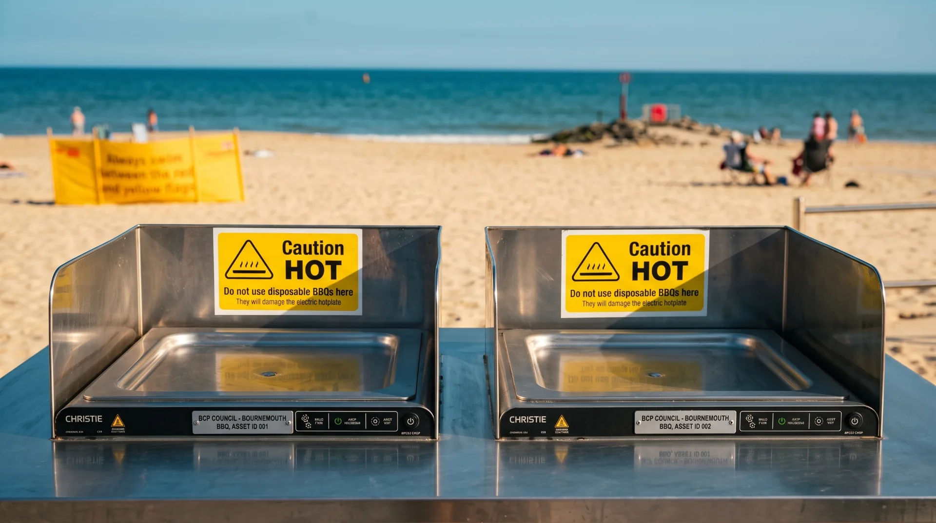 Two electric BBQ stations with caution signs on Bournemouth beach, overlooking the sea and sandy shore.