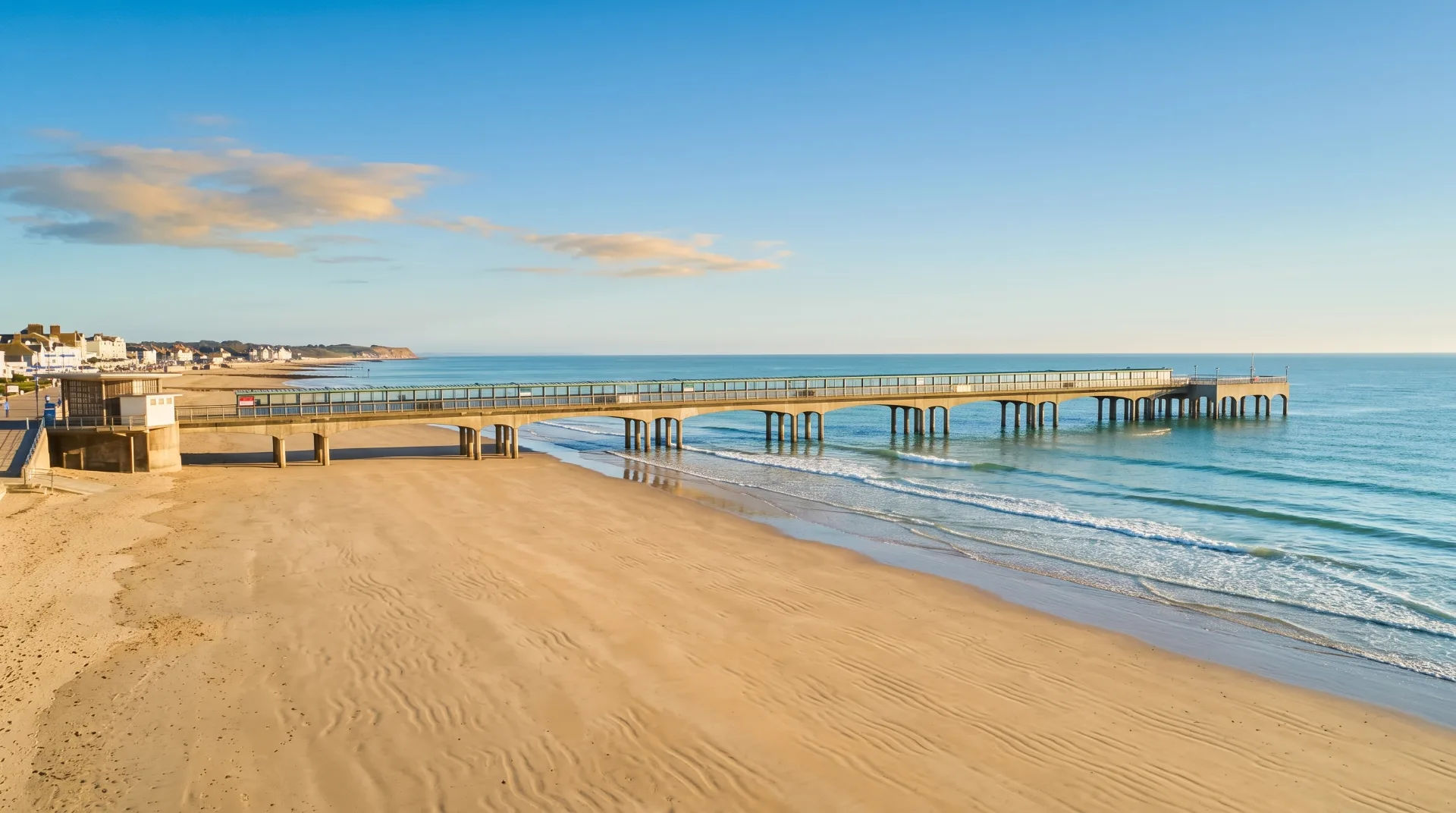 A sandy beach with a pier extending into calm waters under a clear blue sky.