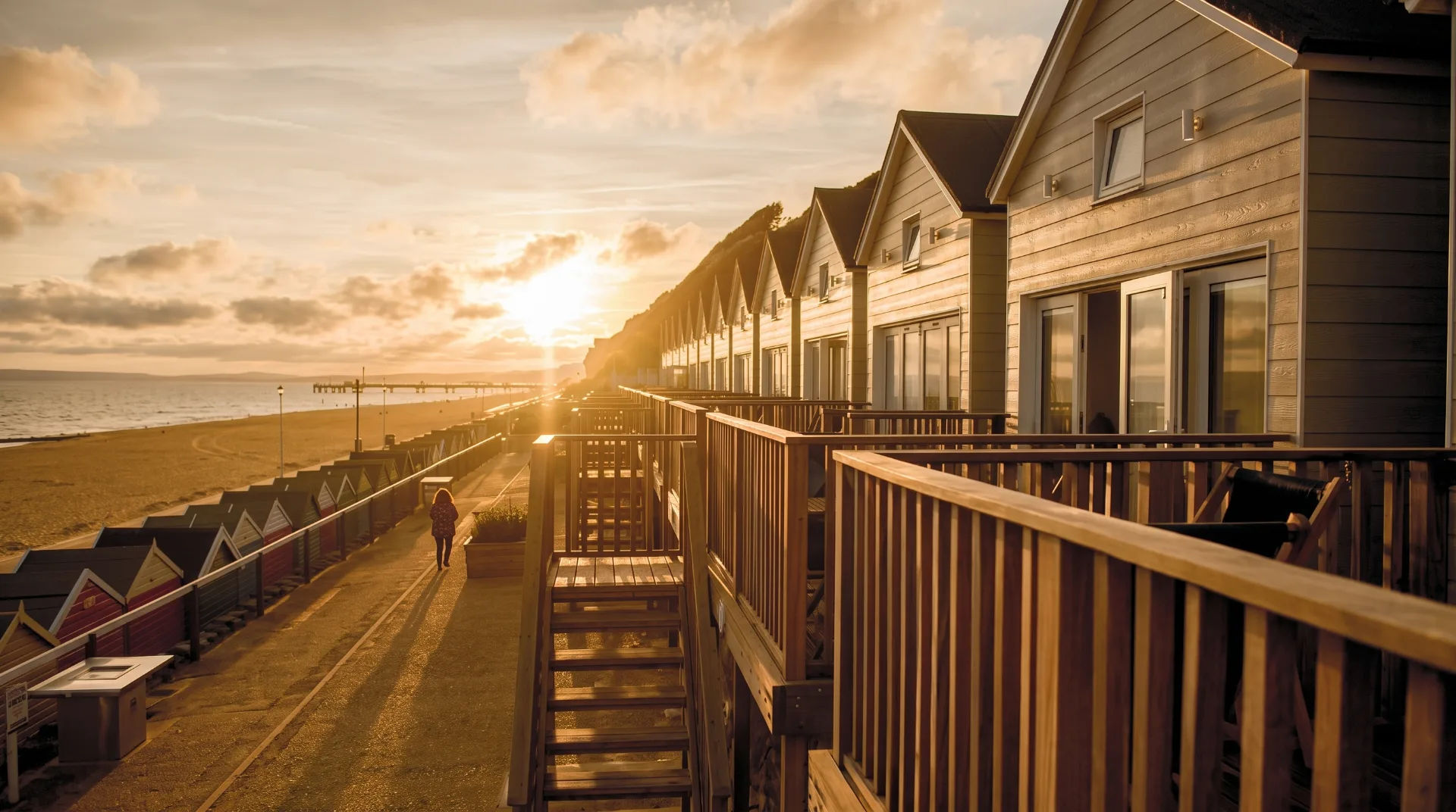 Sunset over beach huts along a sandy beach with a person walking on a path
