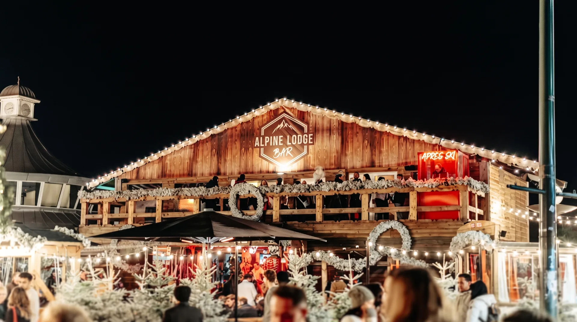 Wooden Alpine Lodge bar with festive lights and people enjoying the market at night