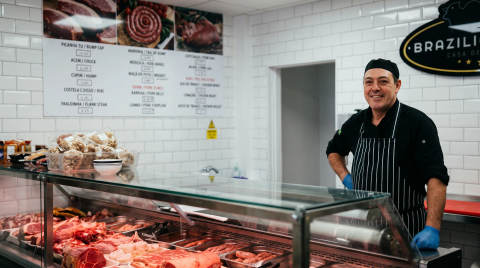 A butcher in a shop standing behind a glass display of meats