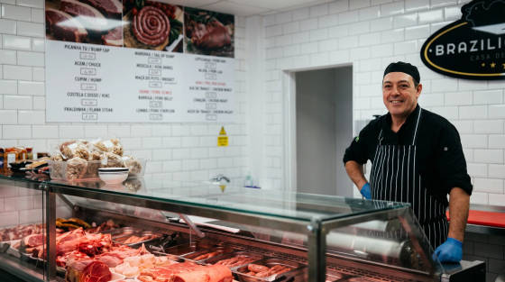 A butcher in a shop standing behind a glass display of meats