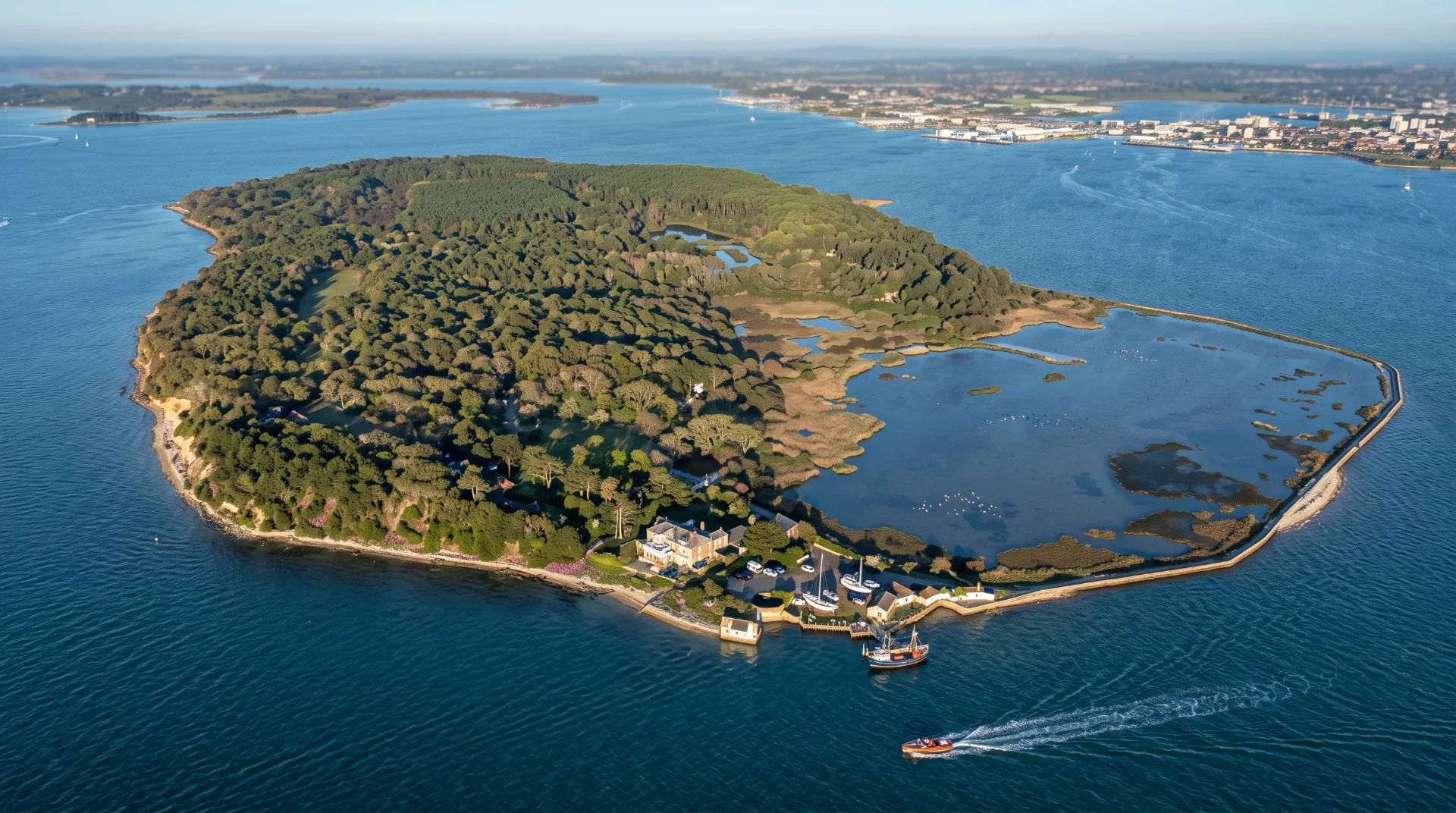 Aerial view of a lush green island surrounded by blue water, with boats and a coastal settlement visible.