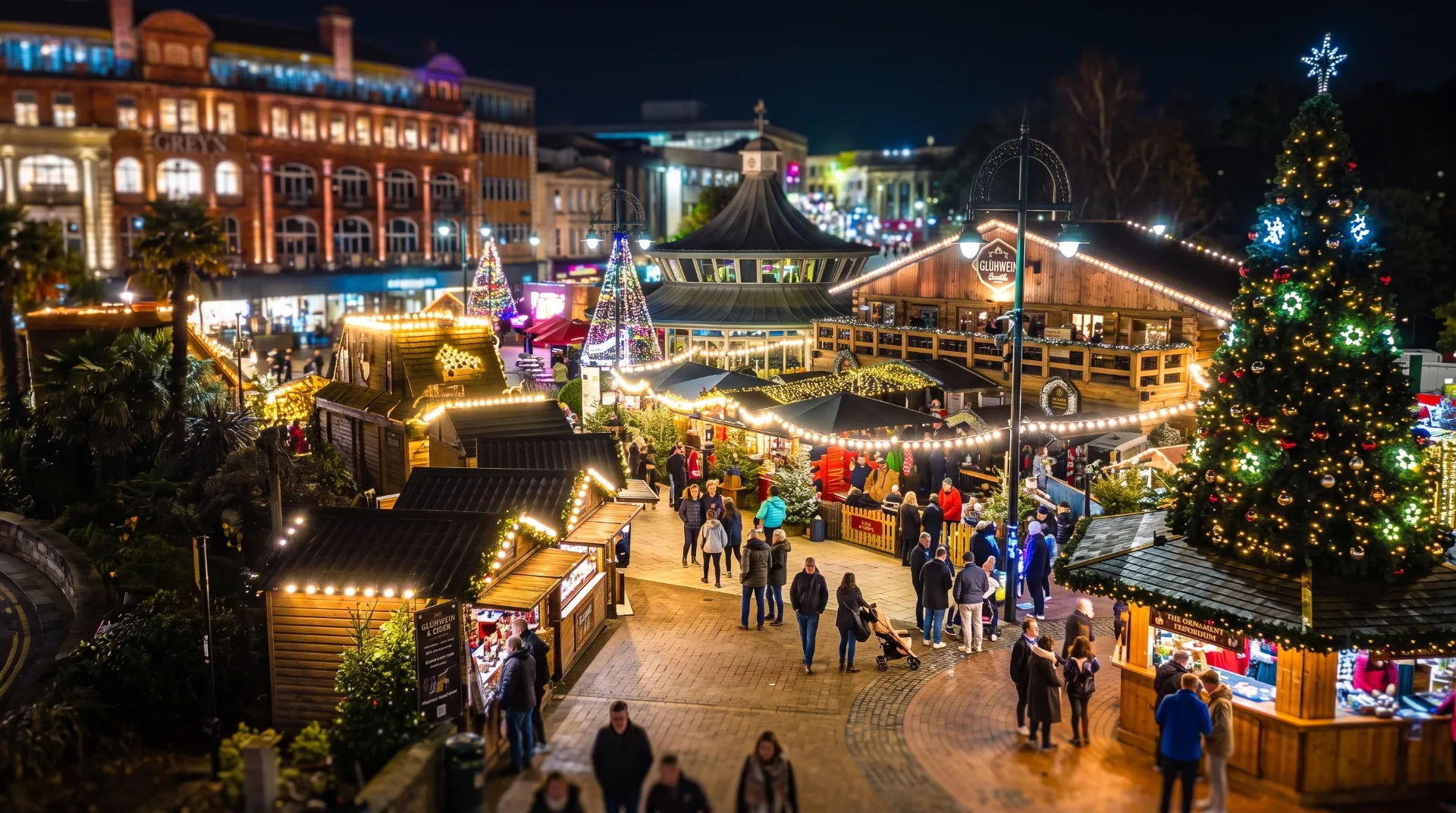 Festively lit Christmas market with wooden stalls, a large decorated tree, and crowds enjoying the evening atmosphere.