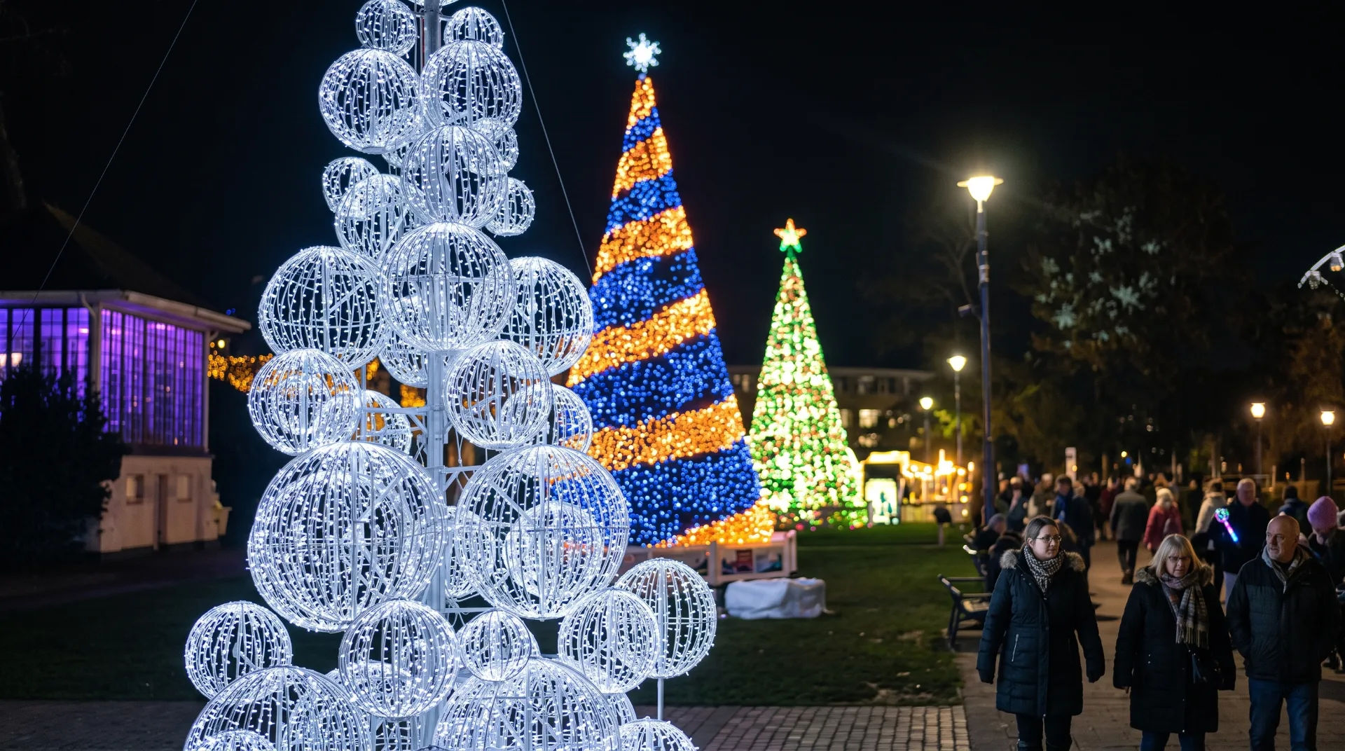 Illuminated Christmas trees and decorations in Lower Gardens at night, with people walking along the path.