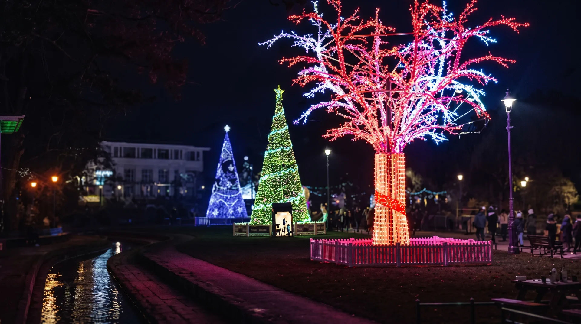 Illuminated Christmas trees and colourful lights in a park at night with visitors walking nearby