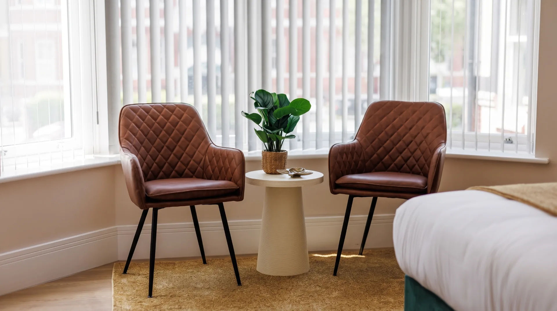 Two stylish brown chairs with a small table and potted plant in a bright room with large windows