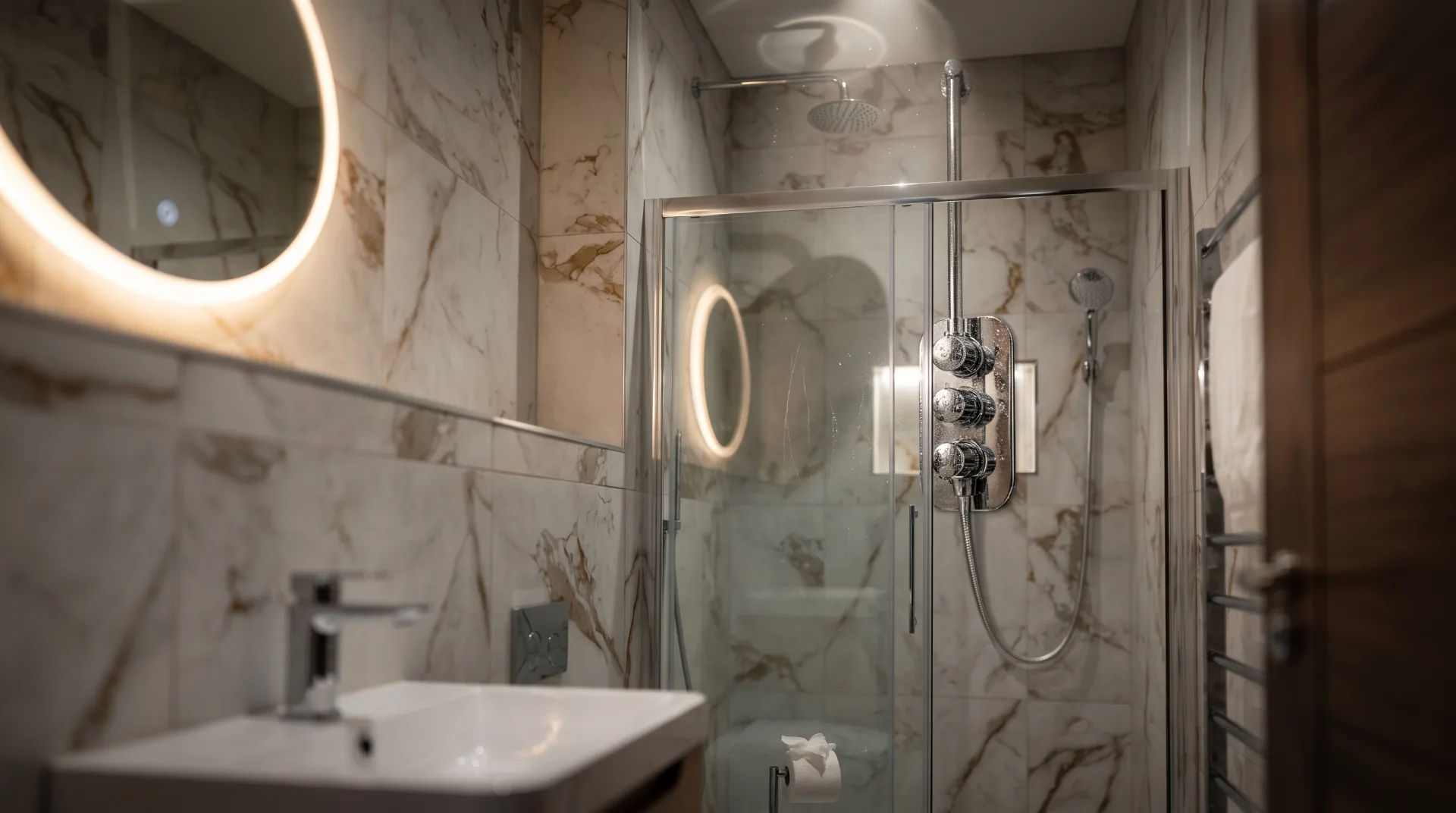 Modern bathroom featuring a glass shower, marble walls, and a circular illuminated mirror