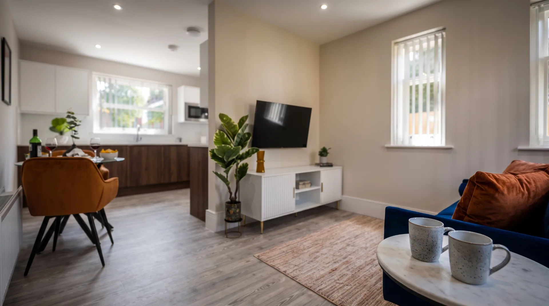 Modern living area in Cliff Manor Apartments with a sofa, TV, dining table, and kitchen area.