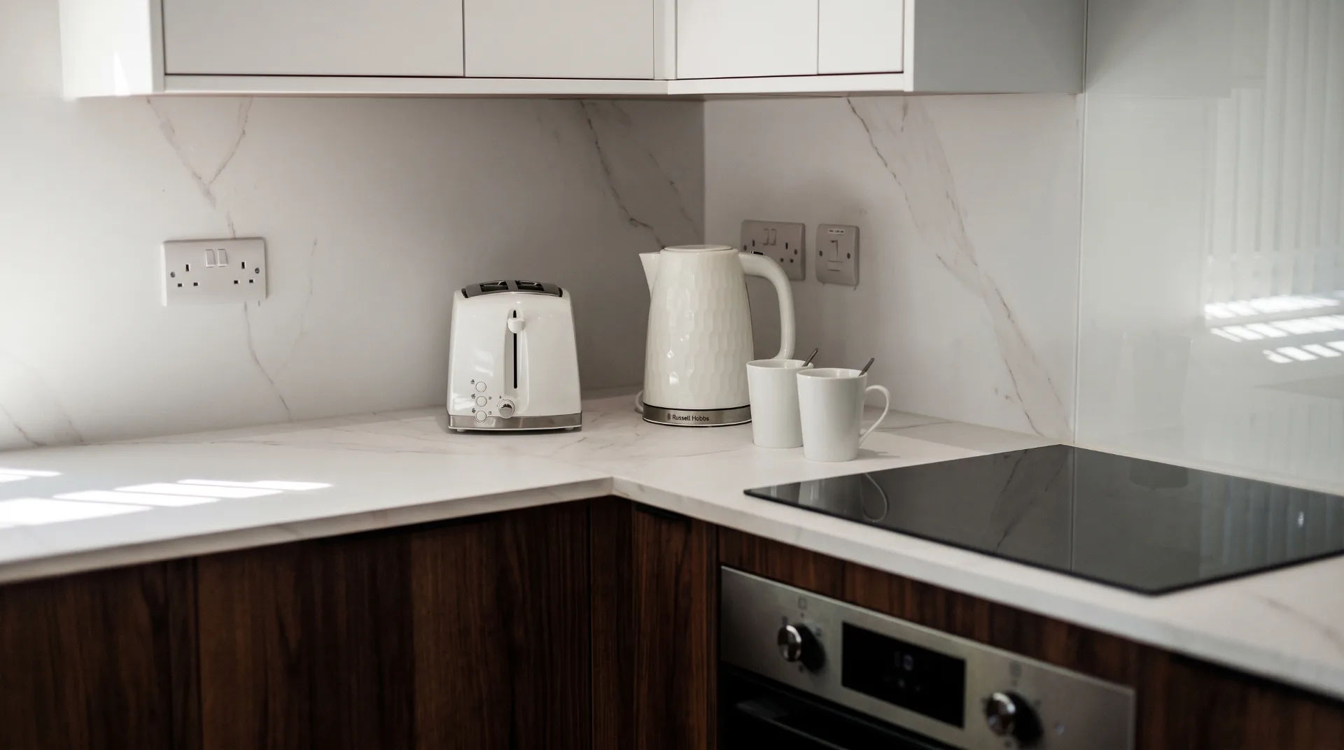 Modern kitchen corner with white kettle, toaster, and two mugs on marble countertop
