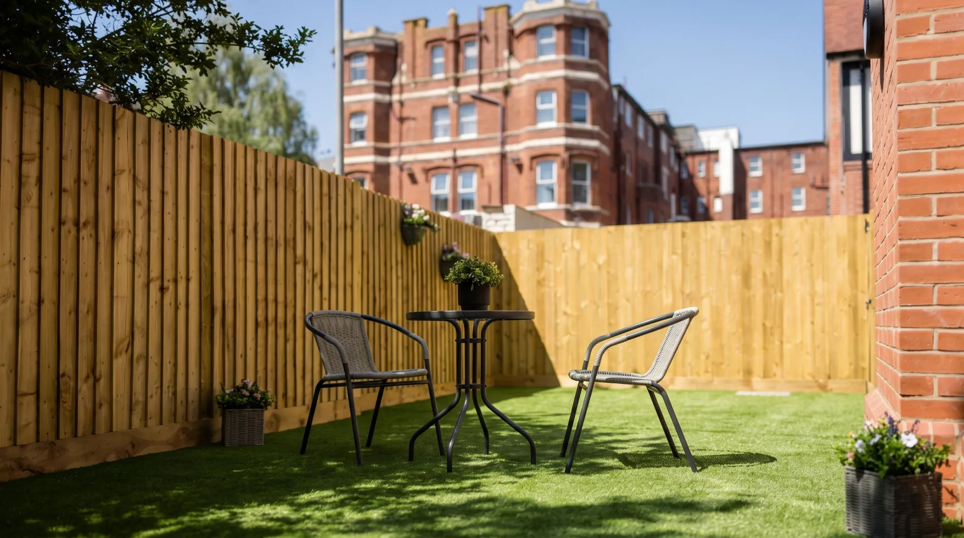 Outdoor seating area with a small table and two chairs, surrounded by wooden fencing and greenery