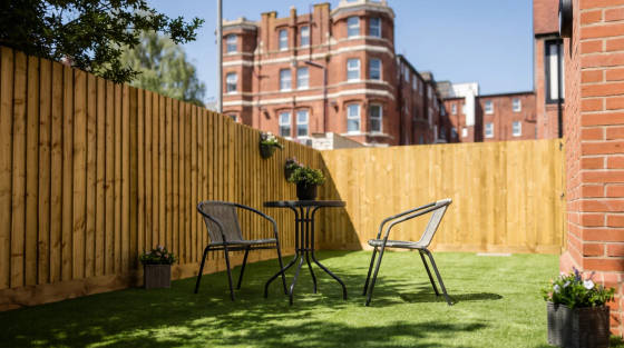 Two chairs and a table on artificial grass surrounded by wooden fencing
