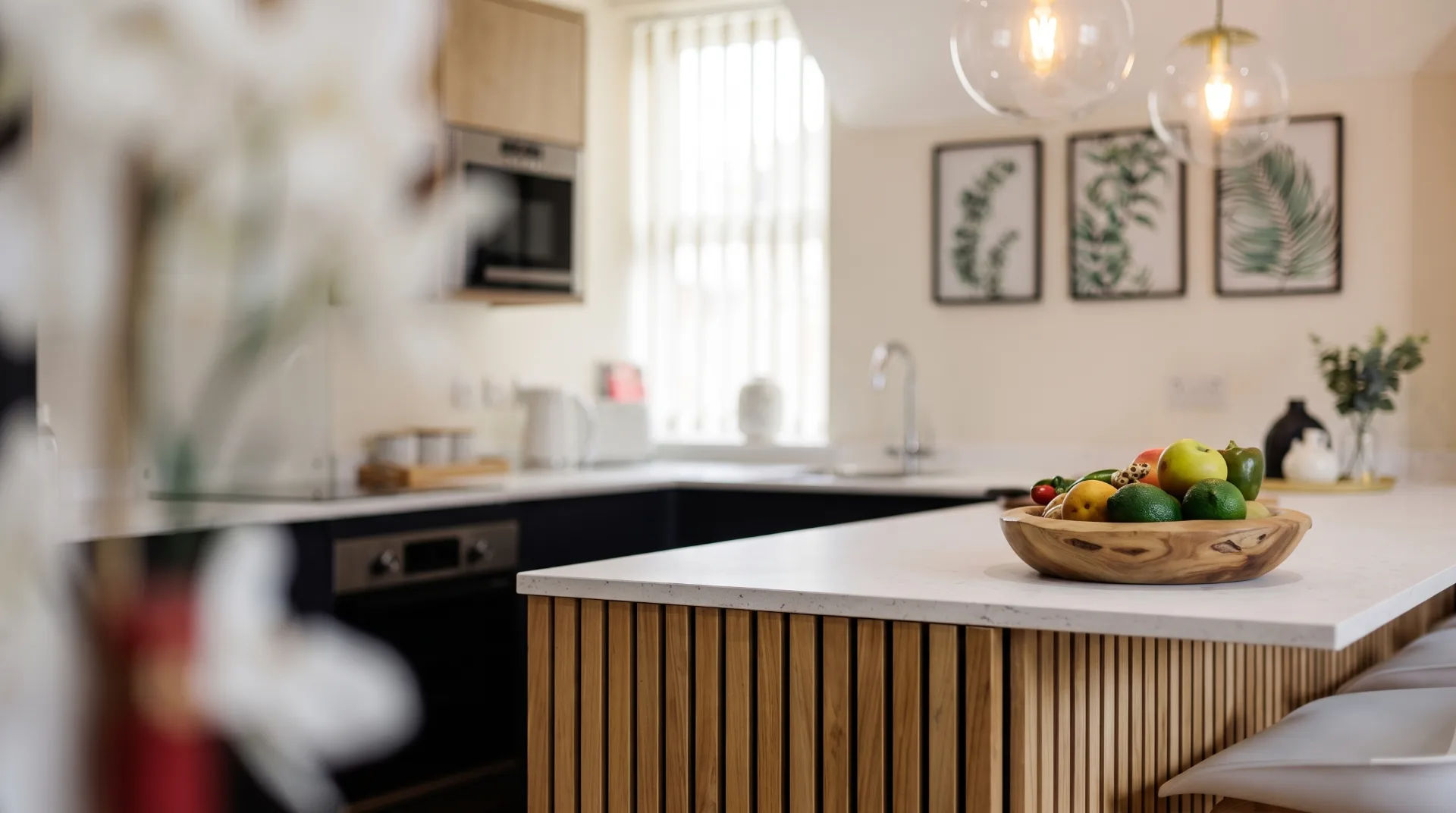 Modern kitchen with wooden island, bowl of fruit, and framed plant artwork on the wall