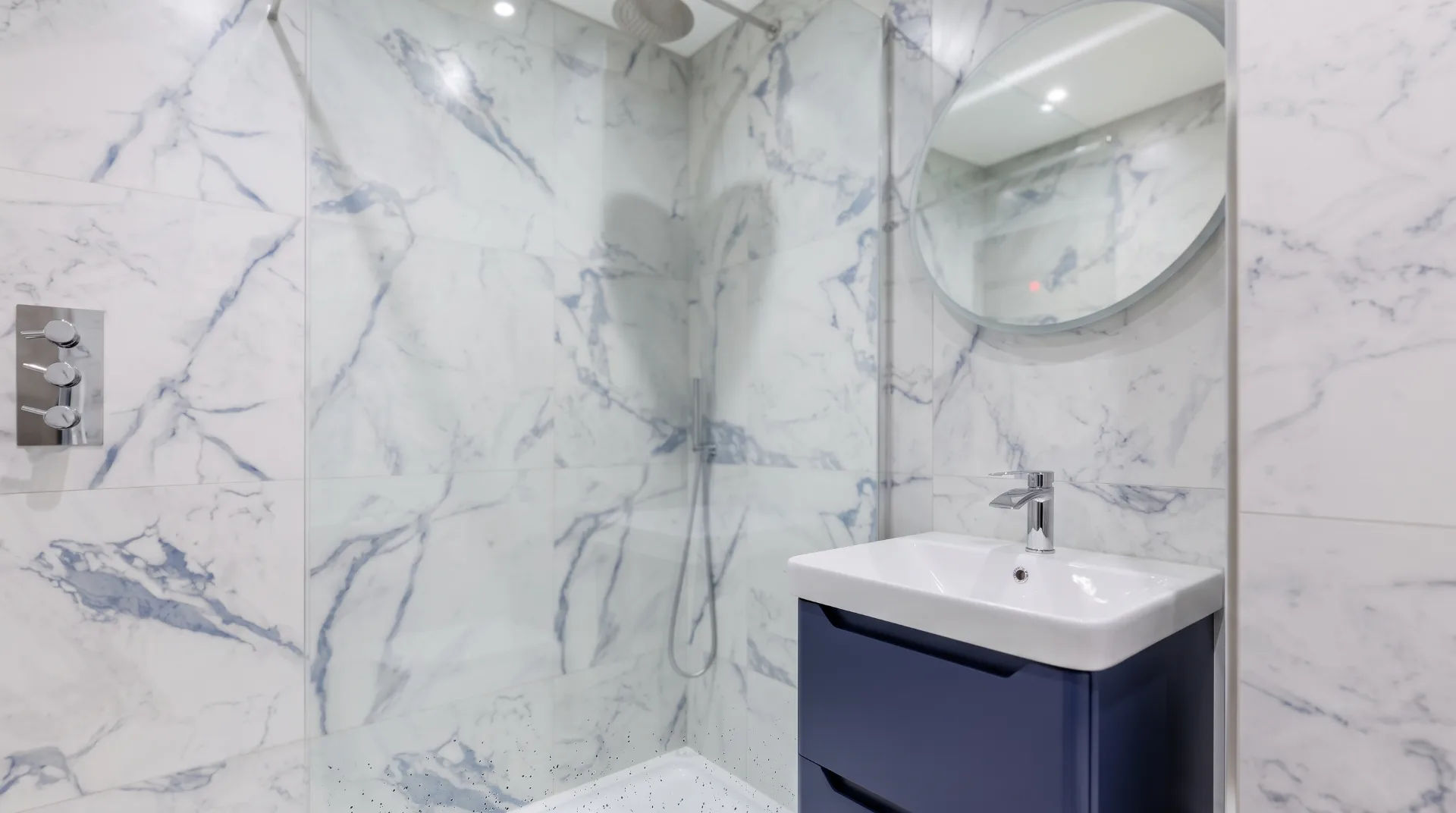 Modern bathroom with marble tiles, a round mirror, and a sleek sink unit.