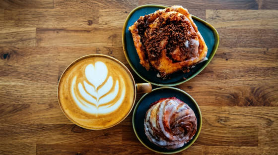 A cup of latte art with two pastries on teal plates