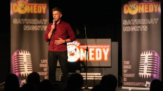 Comedian on stage with microphone and comedy banners in the background