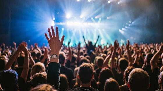 Audience with hands raised at a concert under bright stage lights