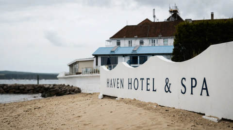 White sign with 'Haven Hotel & Spa' on sandy beach near the water