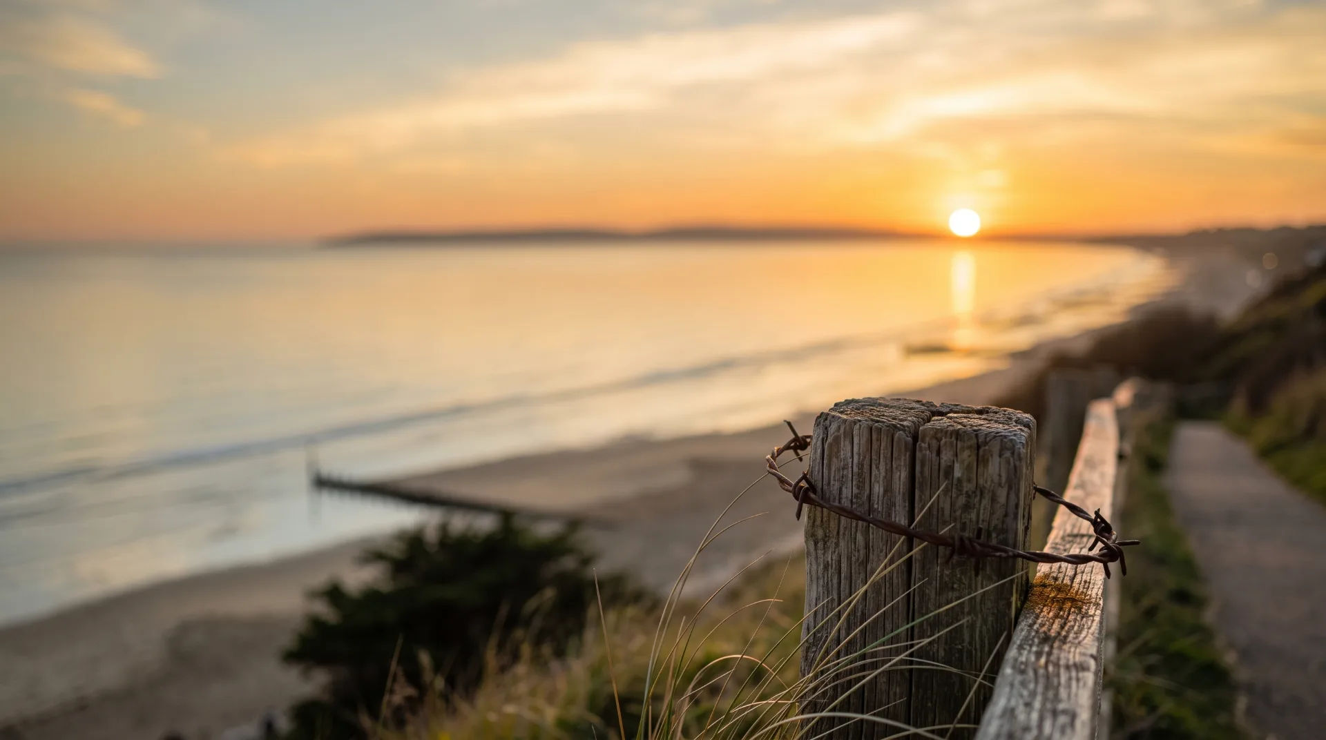 Wooden post with barbed wire at Durley Chine Beach during sunset, with calm sea and sandy shore in background
