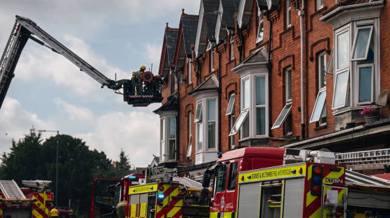 Firefighters in a ladder truck next to red brick houses