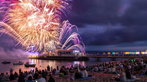 Fireworks illuminate the night sky above Bournemouth Pier with crowds on the beach