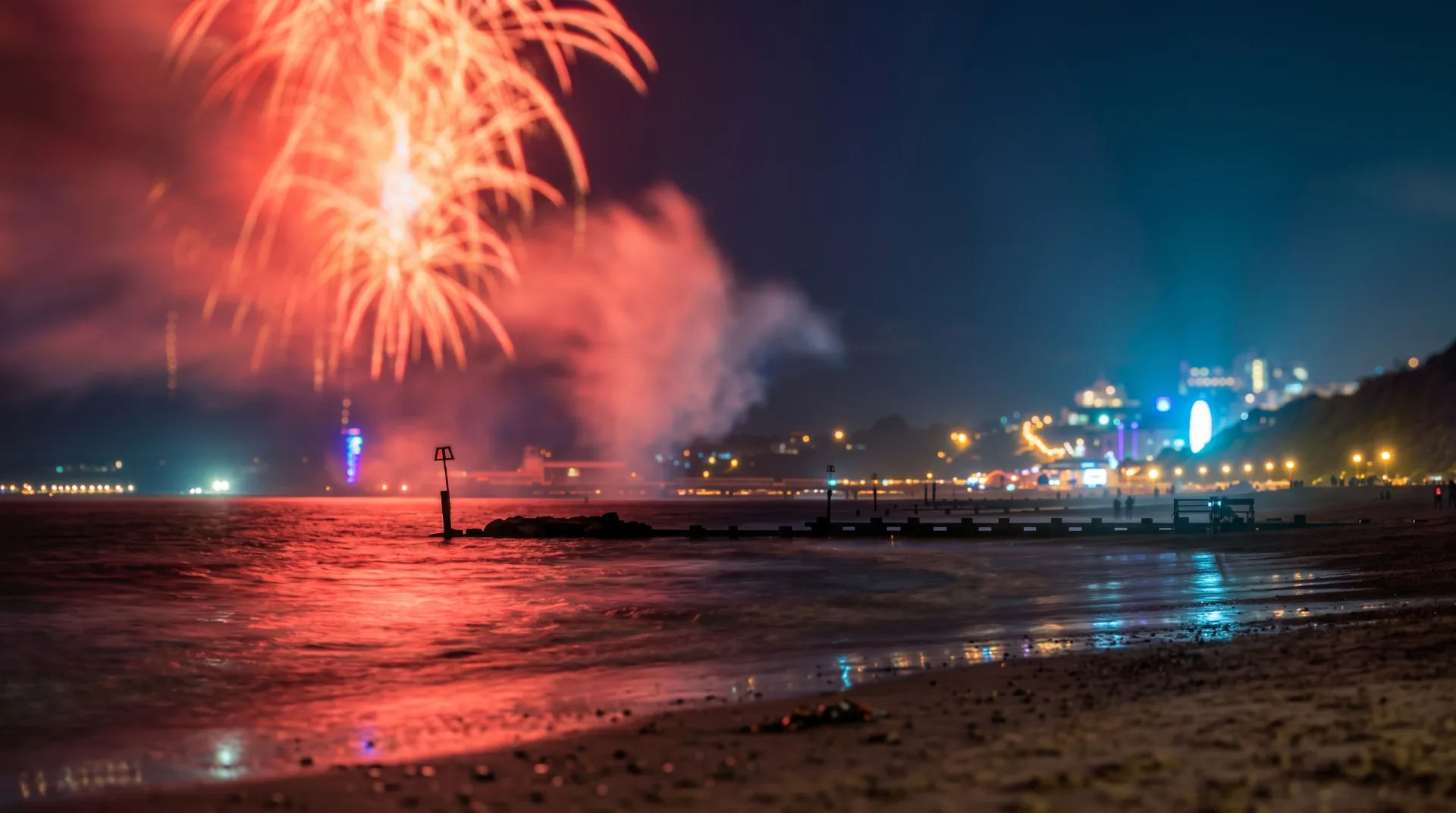 Vibrant fireworks illuminate the night sky above Bournemouth beach, reflecting on the water.