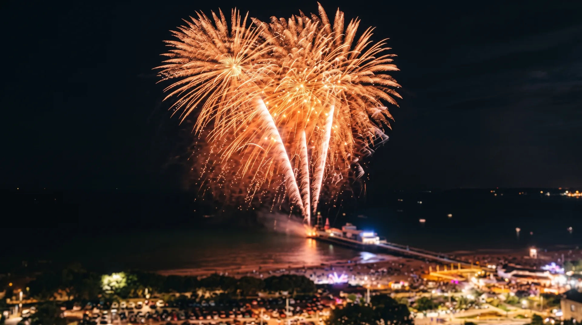 Golden fireworks burst over a marina filled with boats at night, reflecting on the water.
