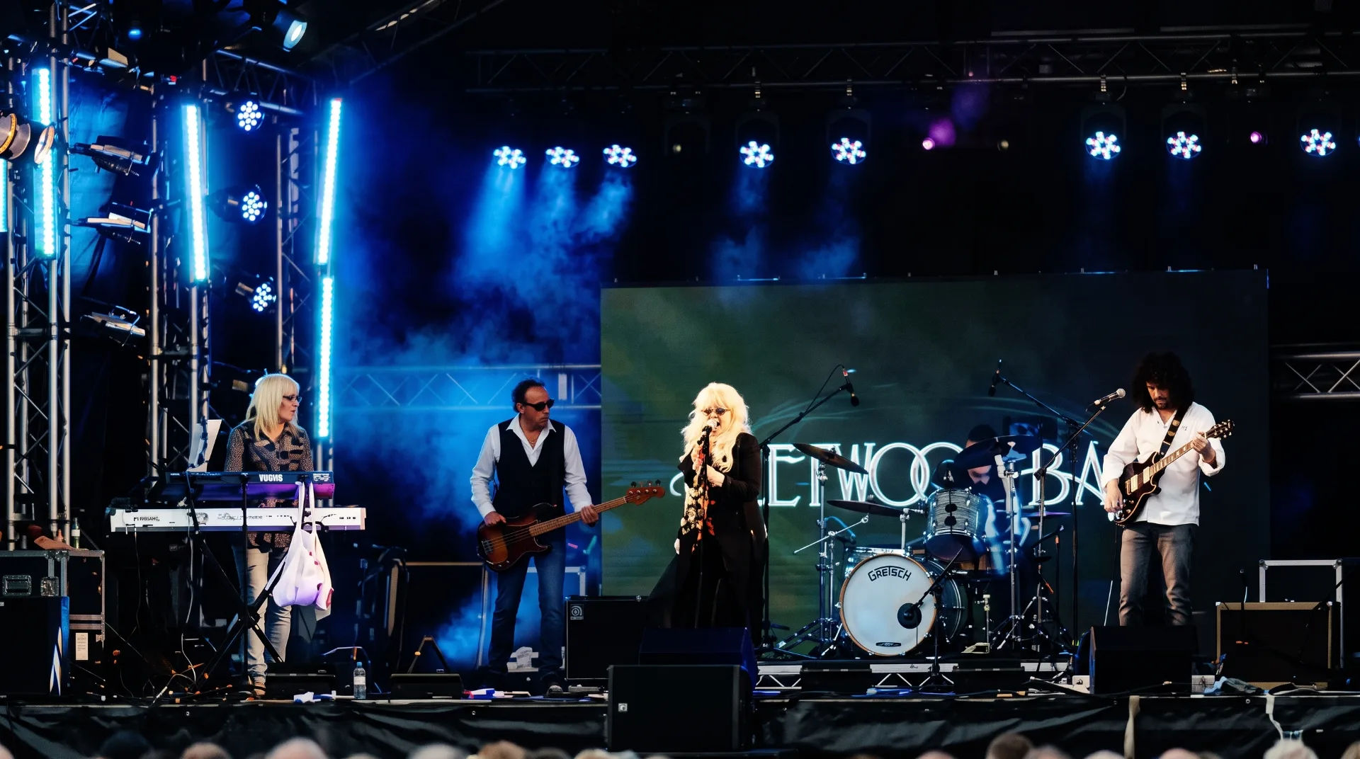 A tribute band performs on stage with vibrant lighting and a large screen behind them.