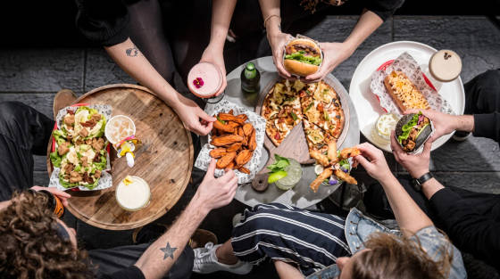 Plates of food and drinks on a table with hands reaching for items